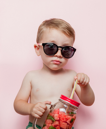 Little boy with Jar of cold fresh lemonade with piece of watermelon and ice on pink background.の写真素材