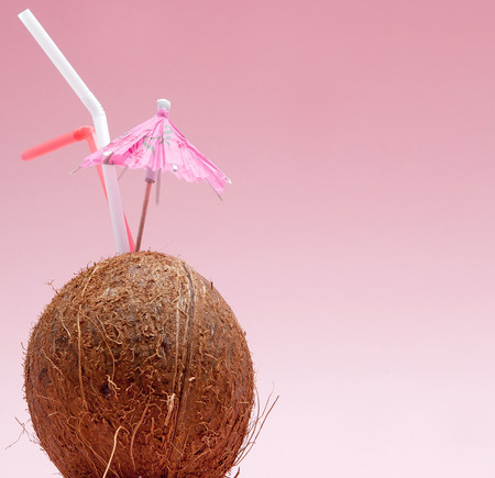 Coconut with drinking straw and umbrella on pink background with copy space.の写真素材