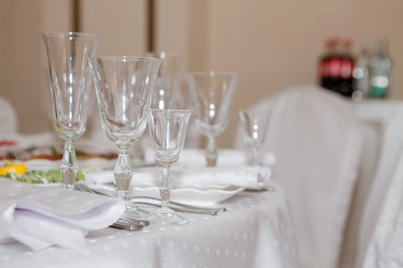 Glasses, flowers, fork, knife, napkin folded in a pyramid, served for dinner in restaurant with cozy...