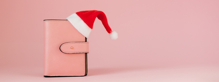 Christmas expenses. Pink leather purse with santa claus cap, gift, fir tree and dollars banknotes on pink background. Christmas shopping. Holiday Sale.の写真素材