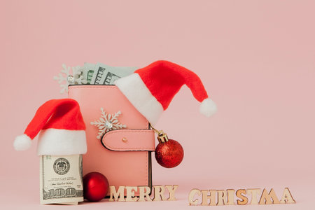 Christmas expenses. Pink leather purse with santa claus cap, gift, fir tree and dollars banknotes on...