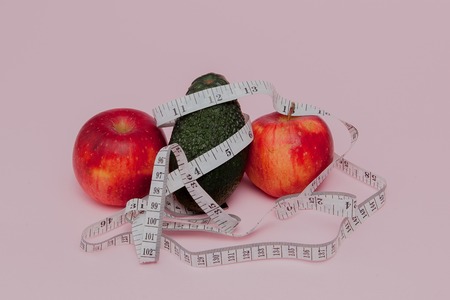 Red apples with a yardstick with avocado on pink background. Diet food concept. Diet food ingredient.の写真素材