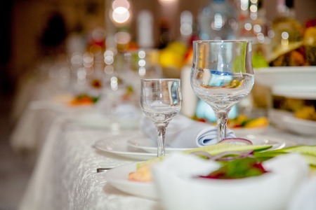 Festive tableware with glasses on a table. Empty glasses stand near plates and forks on banquet table decorated with white tablewear. Festively served table against blurred background in restaurantの写真素材