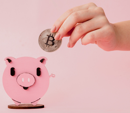 Close up shot hands of woman putting gold bitcoin to pink piggy bank, With copy space for banner design, Shallow depth of field, Select focus on hand.の写真素材
