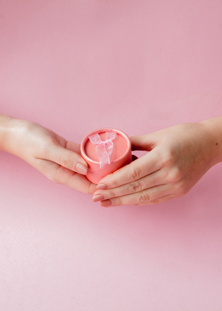 Round pink gift box in women's hands on a pink background. Festive concept for Valentine's day, Mother's day or birthday.の写真素材