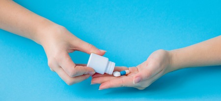 Hands holding white bottle for pills and pills on a blue background.の写真素材