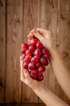 Sweet tasty grapes in graceful woman's hand on wooden background, copy space.の写真素材