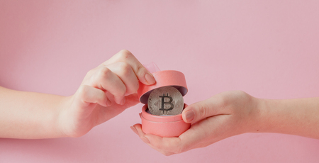 Woman's hands holding bitcoin in pink gift box on a pink background, symbol of virtual money.の写真素材