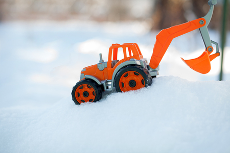 Orange toy tractor with large black wheels close-up, standing in the snow.の写真素材
