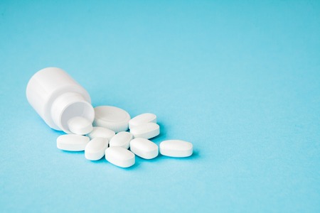 Close up pills spilling out of pill bottle on blue background. Medicine, medical insurance or pharmacy concept.の写真素材