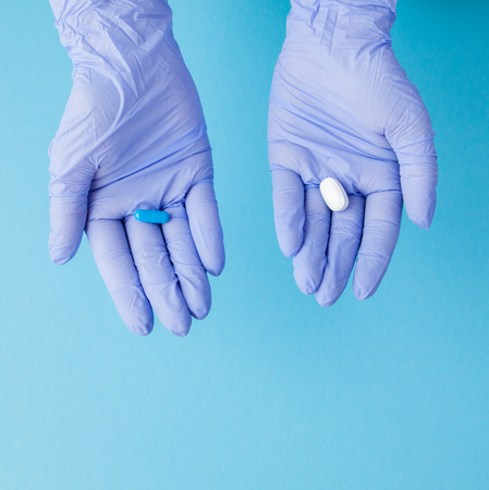 Woman hands in medical gloves giving two big pills. Blue and white. Make your selection.の写真素材