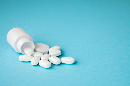 Close up pills spilling out of pill bottle on blue background. Medicine, medical insurance or pharmacy concept.の写真素材