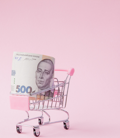 Supermarket Cart Full of UAH banknotes on a pink background with Copy Space. Free trade. money market. Minimalism style. Shop trolley at supermarket. Sale, discount.の写真素材