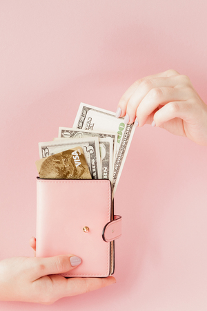 Dollars and pink wallet with credit card in woman's hands on pink background.の写真素材