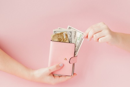 Dollars and pink wallet with credit card in woman's hands on pink background.の写真素材