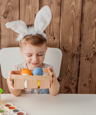 Little boy painting colorful eggs for easter on wooden background.