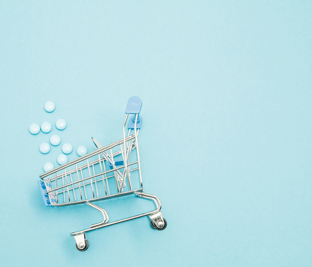 Pills and Shopping trolley on blue background. Creative idea for health care cost, drugstore, health insurance and pharmaceutical company business concept. Copy space.の写真素材