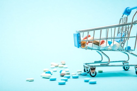 Pills and Shopping trolley on blue background. Creative idea for health care cost, drugstore, health insurance and pharmaceutical company business concept. Copy space.の写真素材