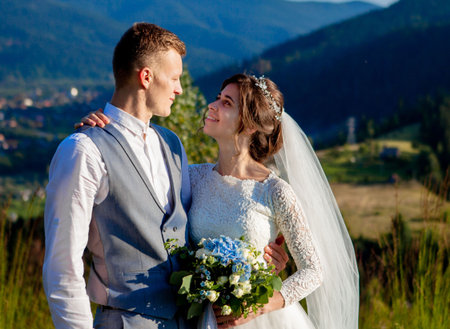Newlyweds smile and hug each other among the meadow on top of the mountain. Wedding walk in the...