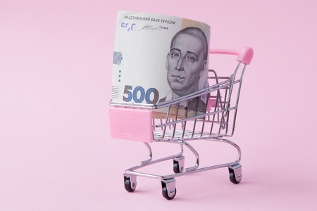 Supermarket Cart Full of UAH banknotes on a pink background with Copy Space. Free trade. money market. Minimalism style. Shop trolley at supermarket. Sale, discount.の写真素材