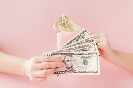 Kyiv, Ukraine - February 22, 2019: Dollars and pink wallet with credit card in woman's hands on pink background.のeditorial素材