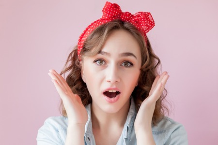 Beautiful young woman with pin-up make-up and hairstyle. Studio shot on pink background.の写真素材