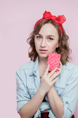 Beautiful young woman with pin-up make-up and hairstyle with cleaning tools on pink background.