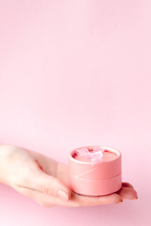 Round pink gift box in women's hands on a pink background. Festive concept for Valentine's day, Mother's day or birthday.の写真素材