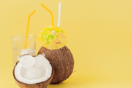 Fresh Coconut cocktail with a straws on yellow background, copy space.