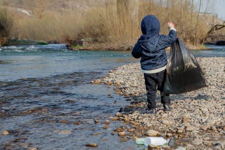 Save environment concept, a little boy collecting garbage and plastic bottles on the beach to dumped into the trashの写真素材