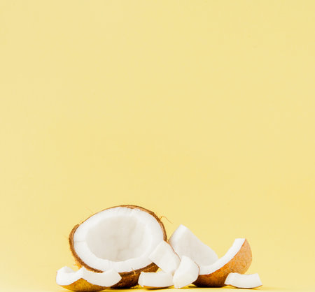 close up fresh coconut pieces isolated on a yellow background, tropical fruit concept, flat lay, pop...