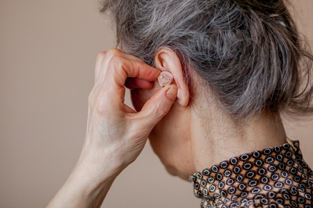closeup senior woman inserting hearing aid in her ears.の写真素材
