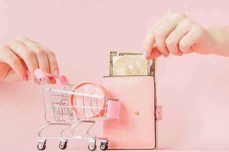 Dollars, gift box and pink wallet with credit card in woman's hands on pink backgroundの写真素材