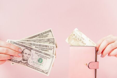 Kyiv, Ukraine - February 22, 2019: Dollars and pink wallet with credit card in woman's hands on pink background.のeditorial素材