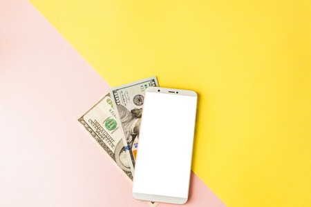 Mobile phone and dollarson pastel pink and yellow background. Minimal style, flatlayの写真素材