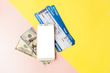 Smartphone, air ticket and dollars on pastel pink and yellow background. Minimal style, flatlayの写真素材