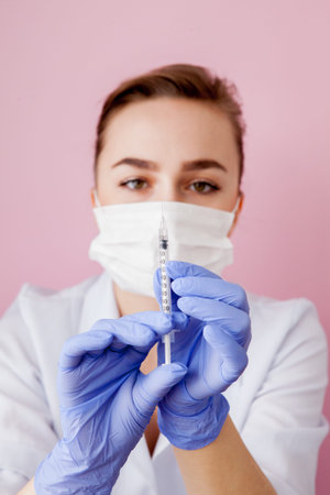 Close up nurse holding a syringe for injection, on pink background.