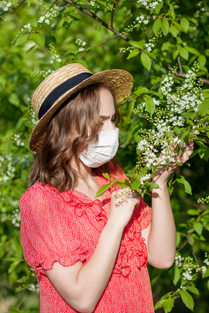 Young girl blowing nose and sneezing in tissue in front of blooming tree. Seasonal allergens affecting people. Beautiful lady has rhinitisの写真素材