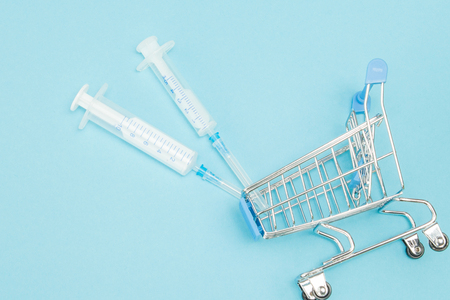 Medical injection in shopping trolley on blue background. Creative idea for health care cost, drugstore, health insurance and pharmaceutical company business concept. Copy space.の写真素材