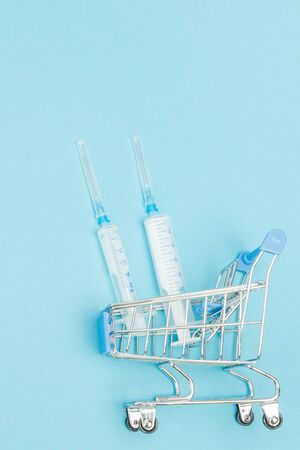 Medical injection in shopping trolley on blue background. Creative idea for health care cost, drugstore, health insurance and pharmaceutical company business concept. Copy space.の写真素材