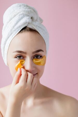 Portrait of Beauty Woman with Eye Patches on pink background. Woman Beauty Face with Mask under Eyes. Beautiful Female with natural Makeup and Gold Cosmetics Collagen Patches on Fresh Facial Skin.の写真素材