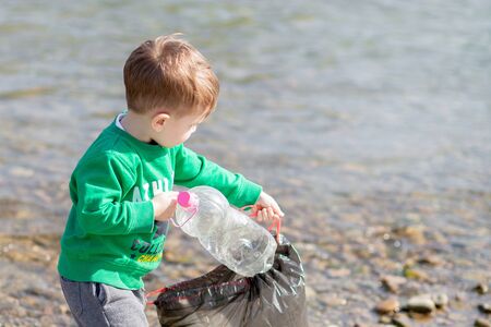 Save environment concept, a little boy collecting garbage and plastic bottles on the beach to dumped into the trashの写真素材
