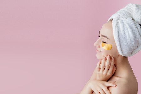 Portrait of Beauty Woman with Eye Patches on pink background. Woman Beauty Face with Mask under Eyes. Beautiful Female with natural Makeup and Gold Cosmetics Collagen Patches on Fresh Facial Skin.の写真素材