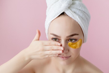 Portrait of Beauty Woman with Eye Patches on pink background. Woman Beauty Face with Mask under Eyes. Beautiful Female with natural Makeup and Gold Cosmetics Collagen Patches on Fresh Facial Skin.の写真素材