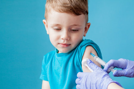 Vaccination concept. Female doctor vaccinating cute little boy on blue background, closeup.