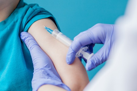 Vaccination concept. Female doctor vaccinating cute little boy on blue background, closeup.の写真素材