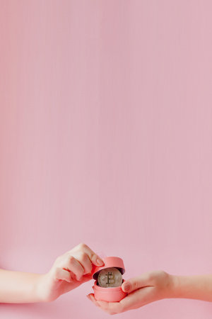 Woman's hands holding bitcoin in pink gift box on a pink background, symbol of virtual money.の写真素材
