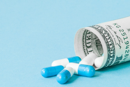 Money dollar rolled up with pills flowing out isolated on blue background, high costs of expensive medication concept. Copy space.の写真素材
