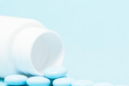 Blue pills and pill bottle on blue background.