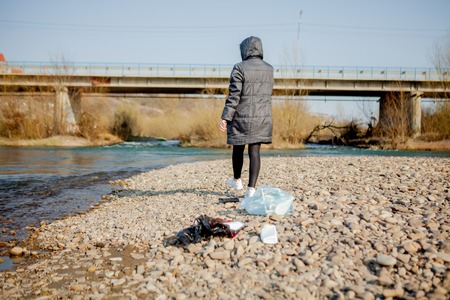 Young woman collecting plastic trash from the beach and putting it into black plastic bags for recycle. Cleaning and recycling conceptの写真素材